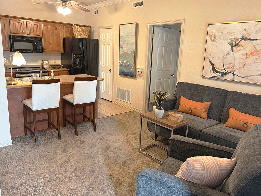 A living room with a grey couch and a kitchen area with a microwave and oven.